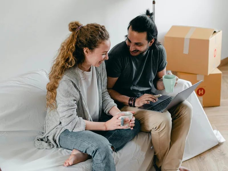 Couple on a sofa with a laptop beside moving boxes