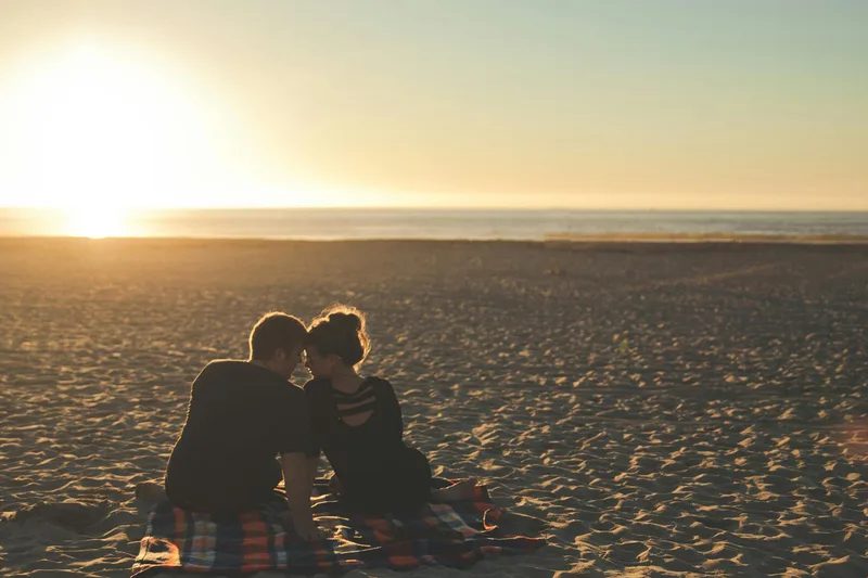 Two people sitting together on a beach at sunset.