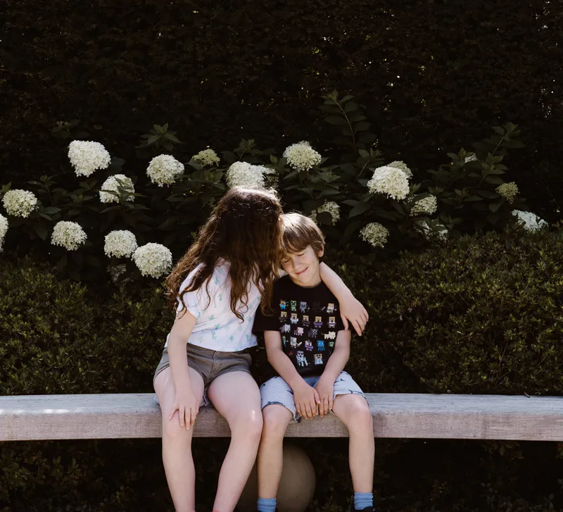 Two children sitting together on a garden bench.