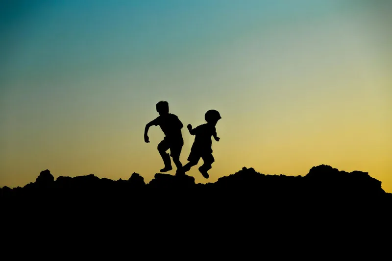 Silhouettes of two children jumping outdoors at sunset