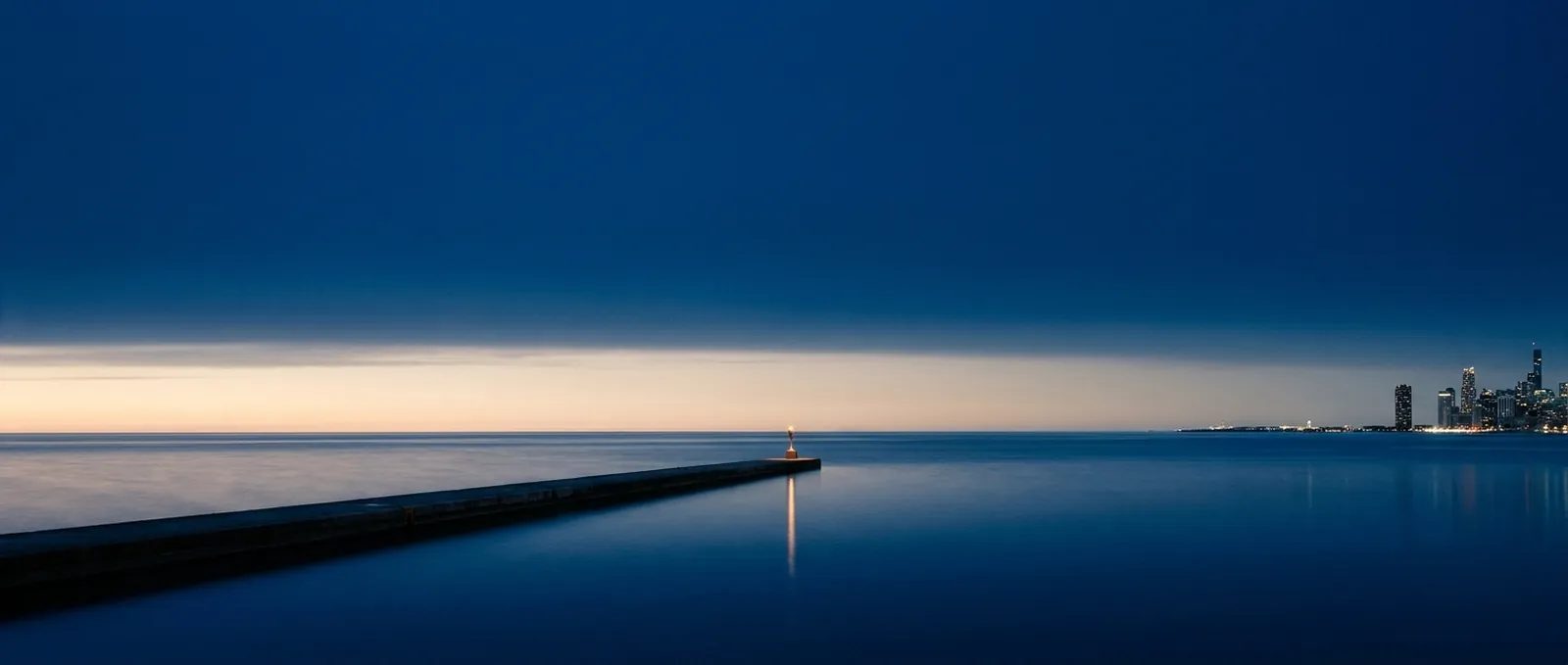 Illustration: Lake Michigan at blue hour, a long breakwater with a single light and the Chicago skyline small on the horizon