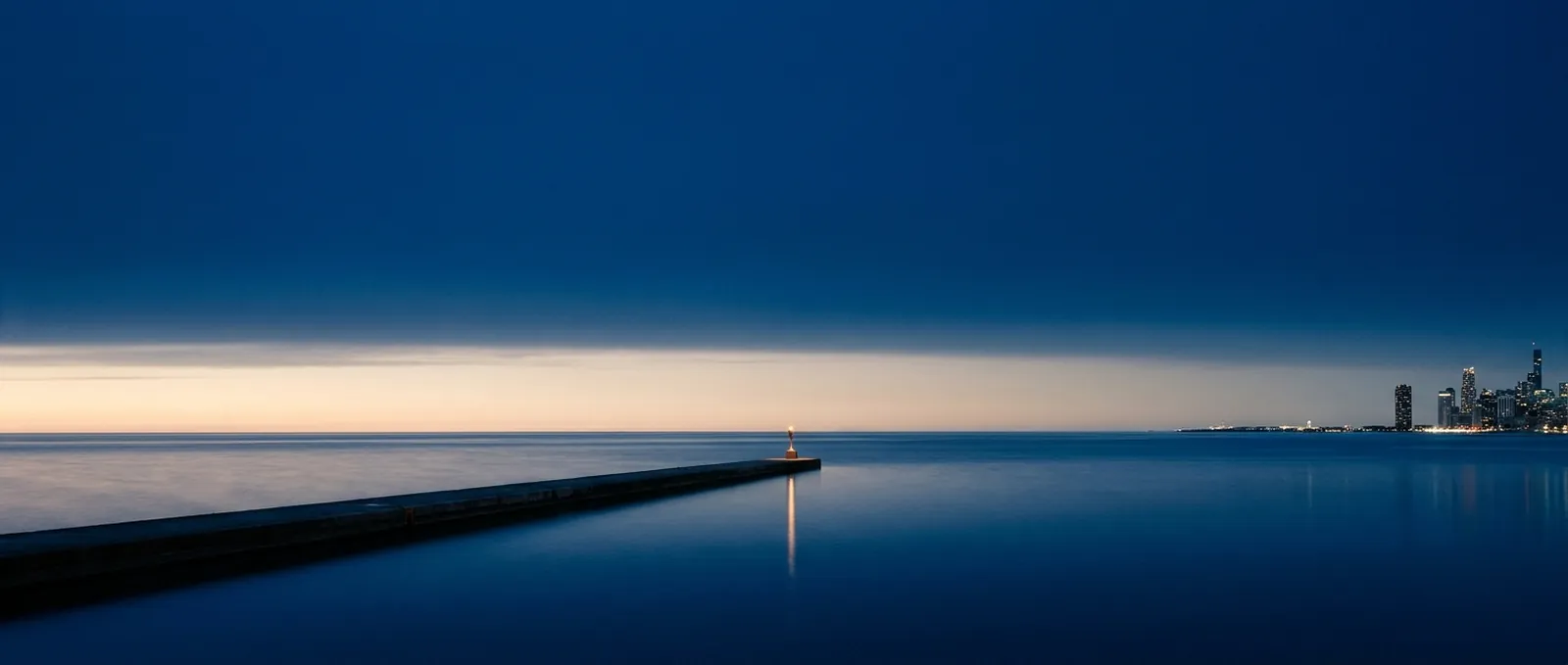 Illustration: Lake Michigan at blue hour, a long breakwater with a single light and the Chicago skyline small on the horizon