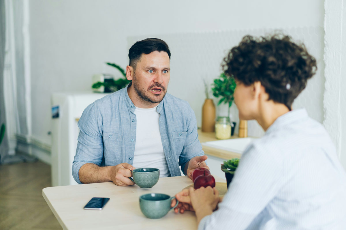 Two adults talking across a kitchen table.