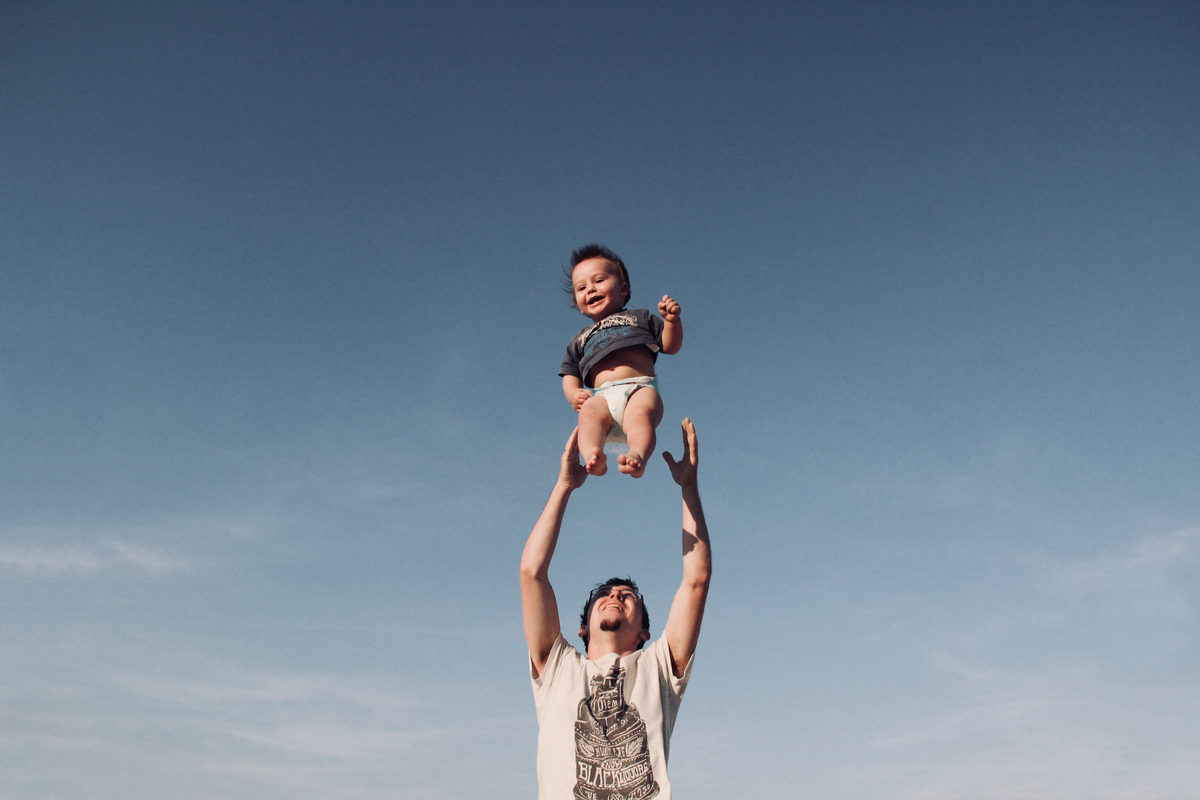 Un adulto lanza hacia arriba a un niño pequeño sonriente al aire libre.