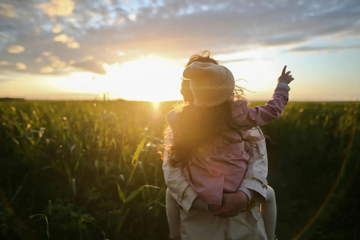Adult holding a child outdoors at sunset