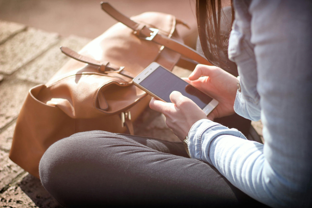 Persona usando un teléfono inteligente junto a un bolso marrón
