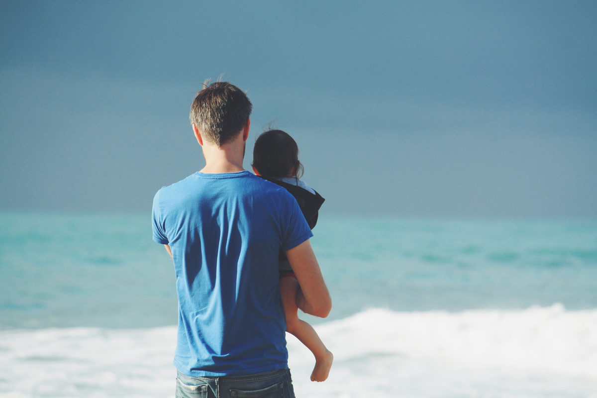 An adult holding a child beside the sea.