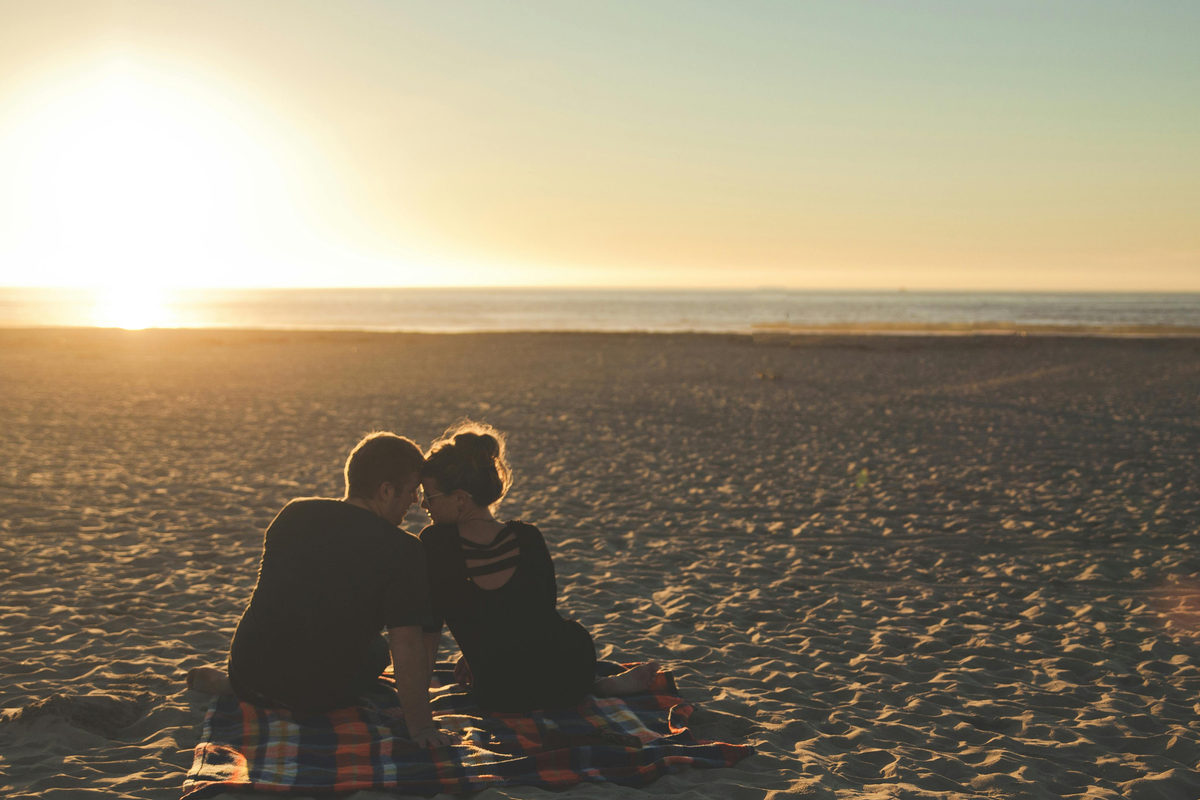 Dos personas sentadas juntas en una playa al atardecer.