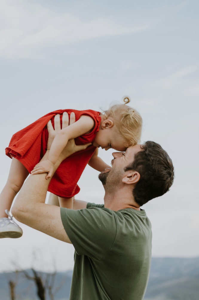 Adult lifting a smiling toddler outdoors