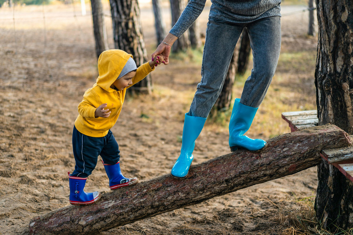 Adult holding a child’s hand while balancing on a fallen tree