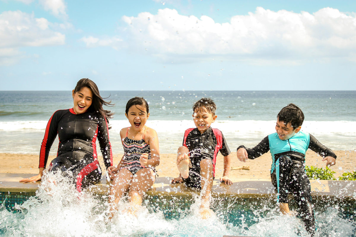 Un adulto y tres niños chapoteando en el agua junto a una playa