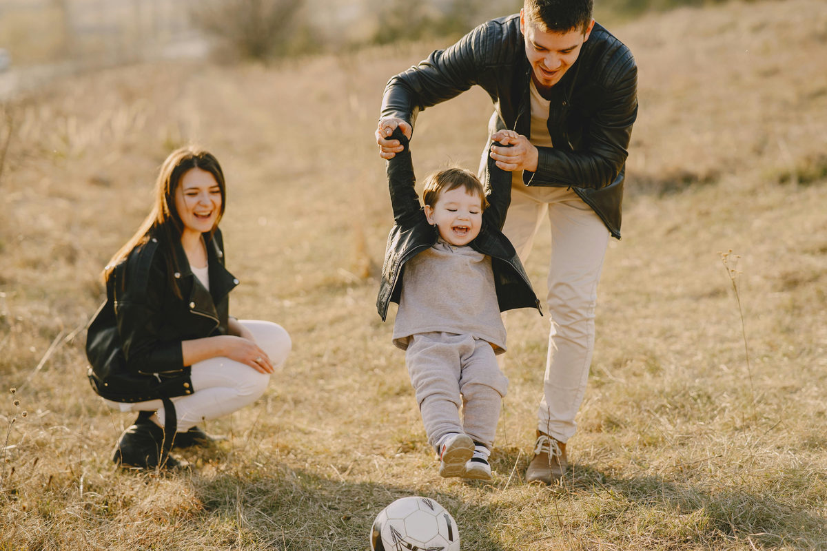 Two adults playing ball with a child outdoors.