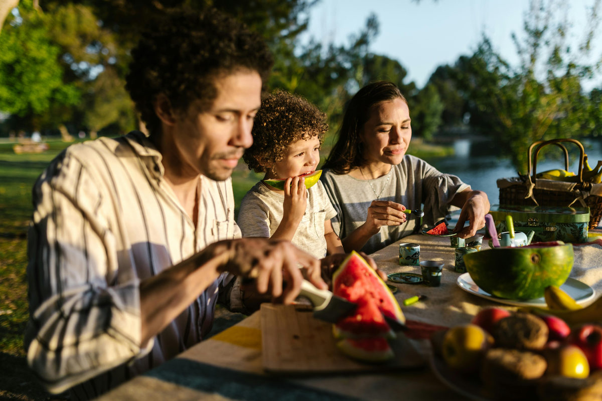 Dos adultos y un niño compartiendo fruta en una mesa al aire libre
