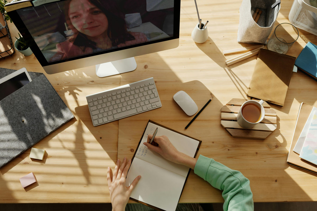 Una reunión por video en una computadora junto a un cuaderno.