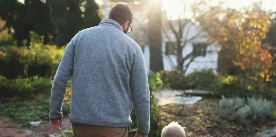 An adult and a young child seen from behind outdoors.