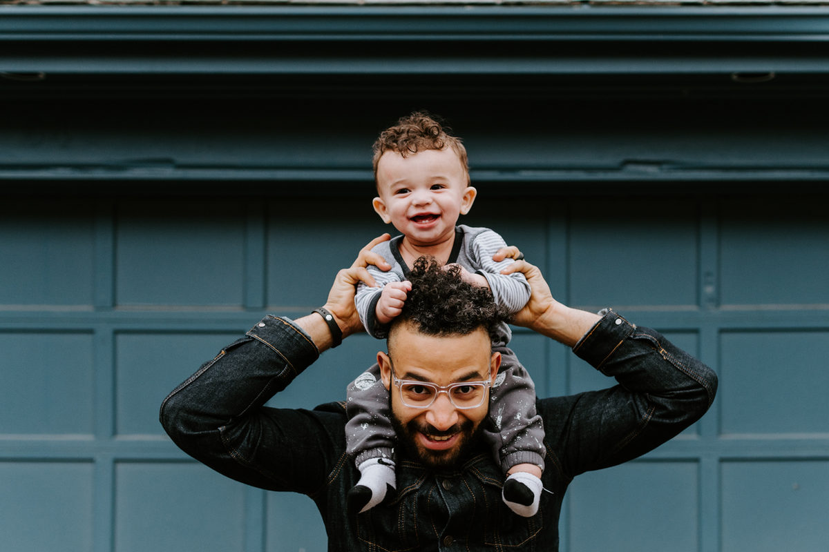 An adult carrying a smiling child on their shoulders.