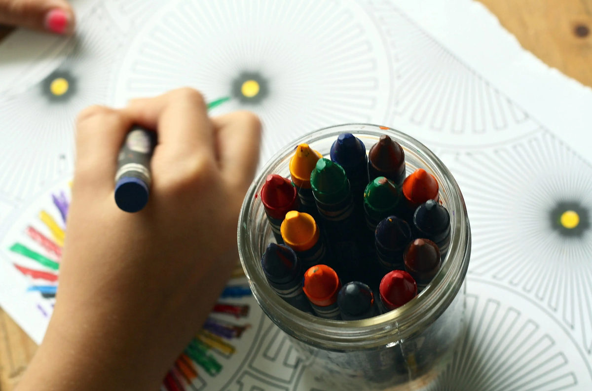 Mano coloreando una página con diseños junto a un frasco de crayones