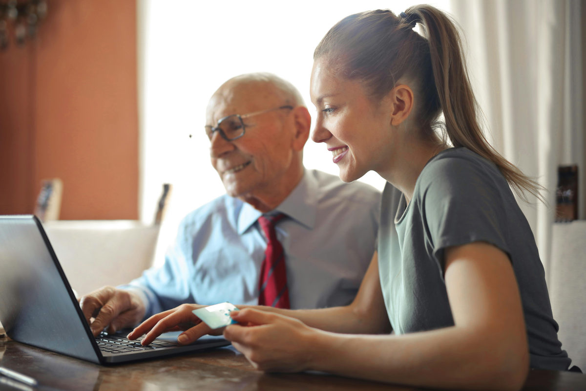 Dos adultos mirando una computadora portátil mientras uno sostiene una tarjeta de pago.