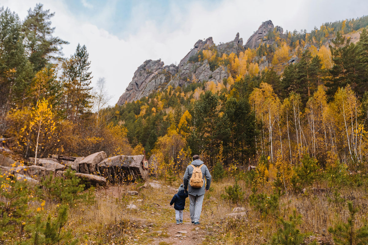 An adult and child hiking through an autumn forest.