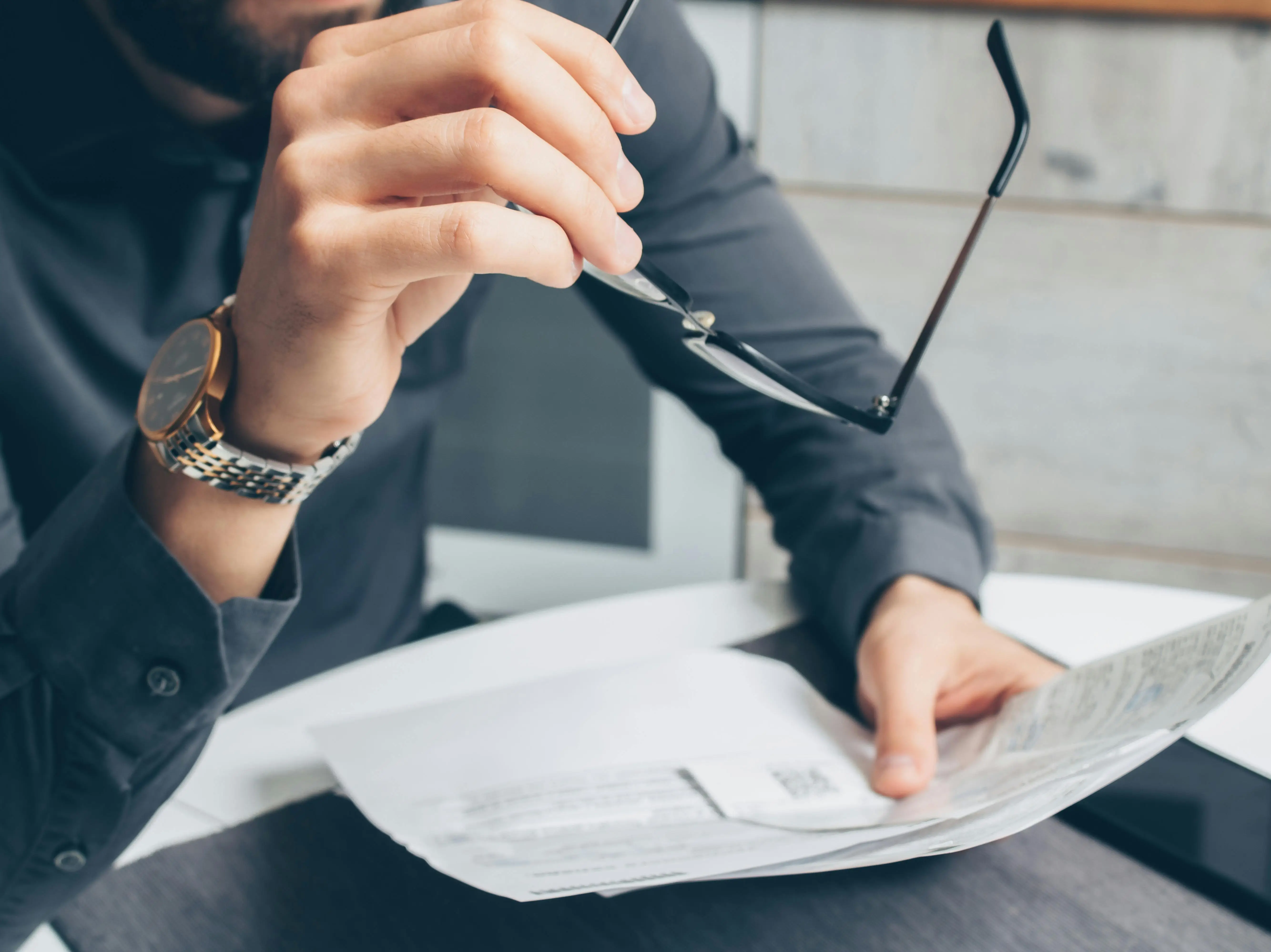 Person holding eyeglasses while reviewing papers.