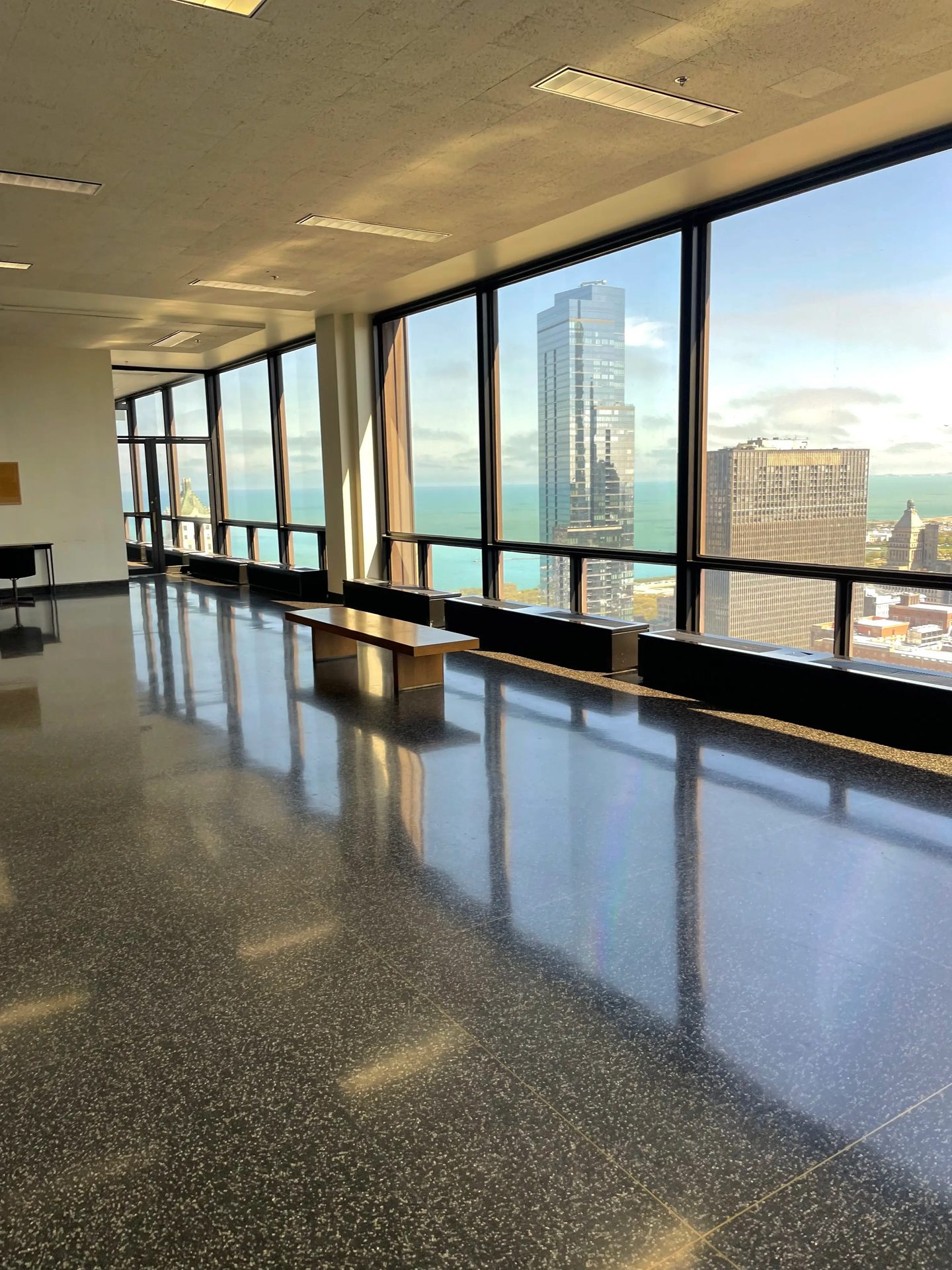 A sunlit interior corridor with windows overlooking city buildings.