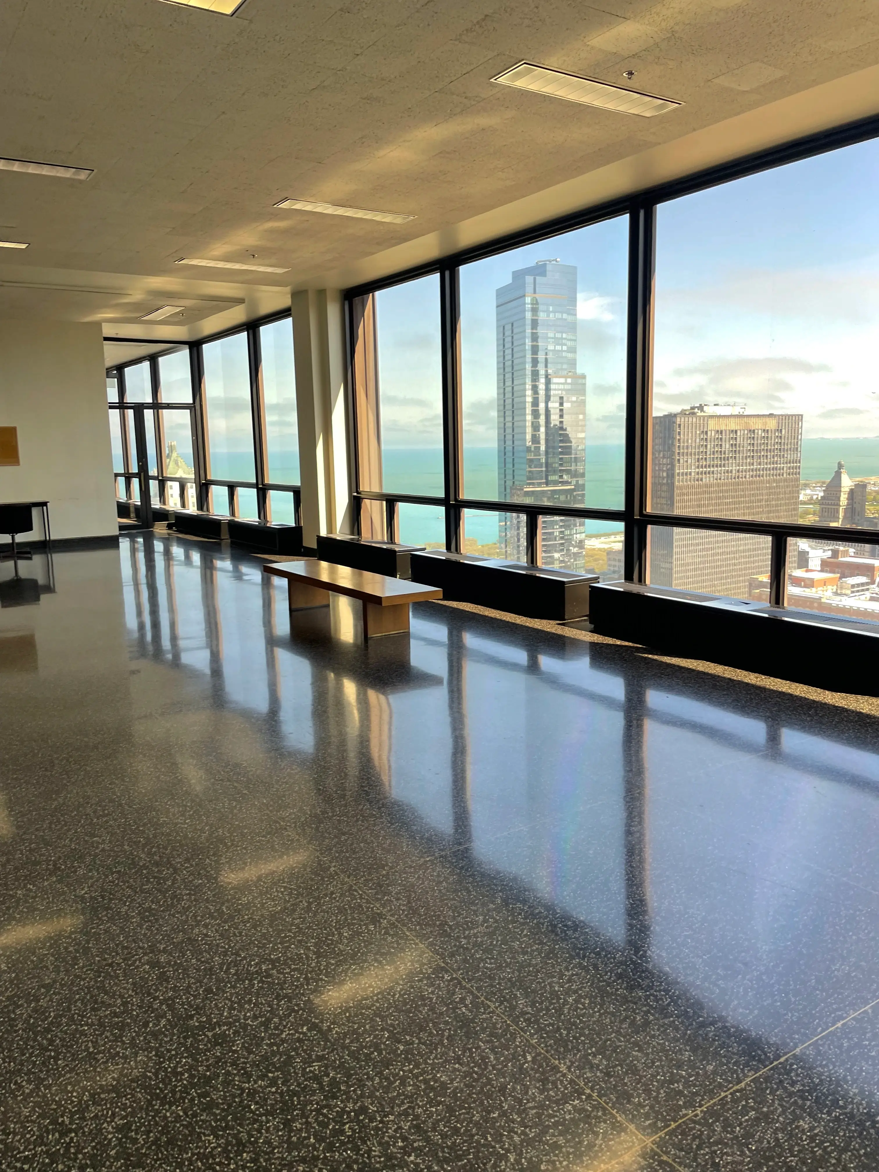 A sunlit interior corridor with windows overlooking city buildings.