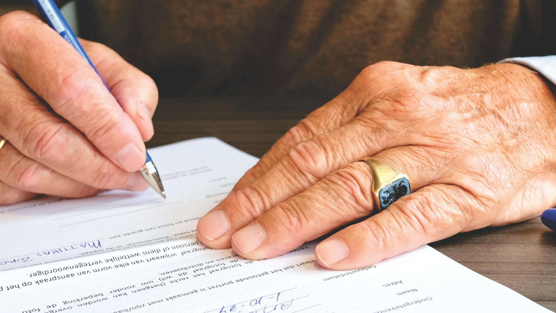 Close-up of a person signing a document with a blue pen.