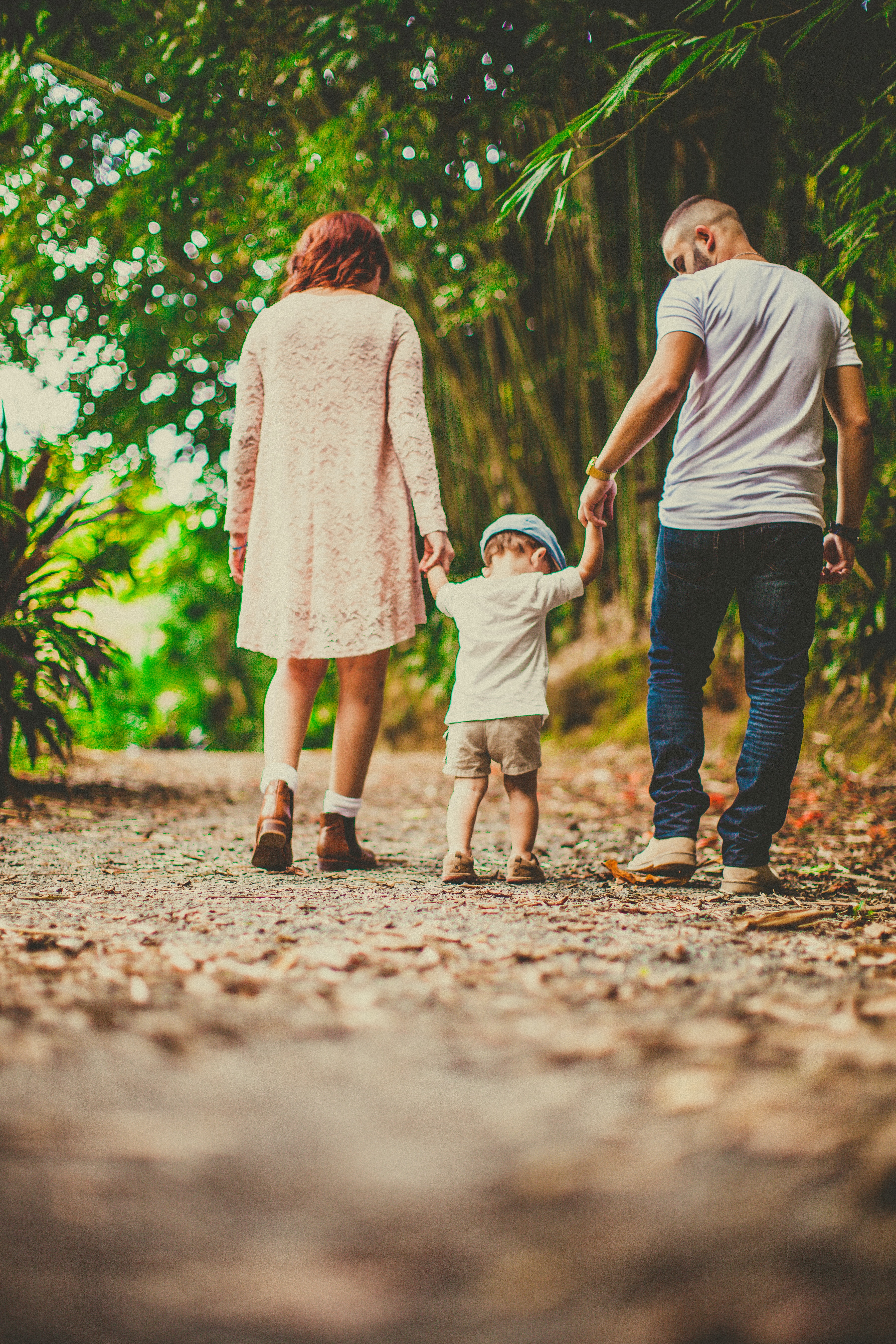 Dos adultos tomando de las manos a un niño pequeño en un sendero arbolado.
