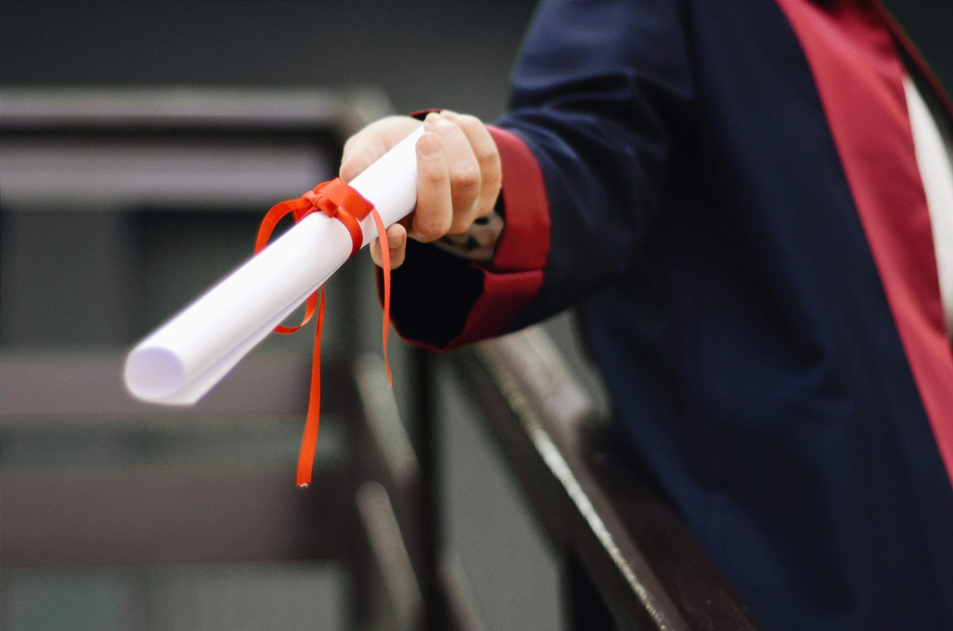 Graduate in a gown holding a rolled diploma tied with a red ribbon