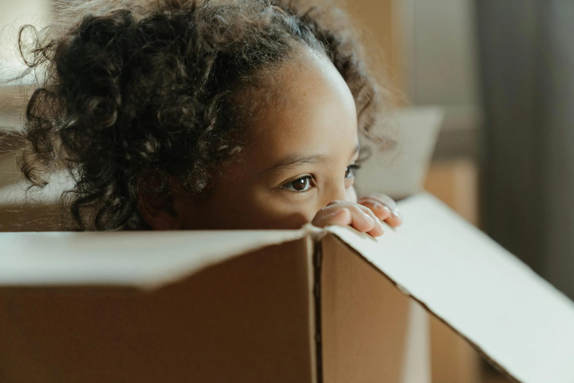 A young child peeking over the edge of a cardboard box.