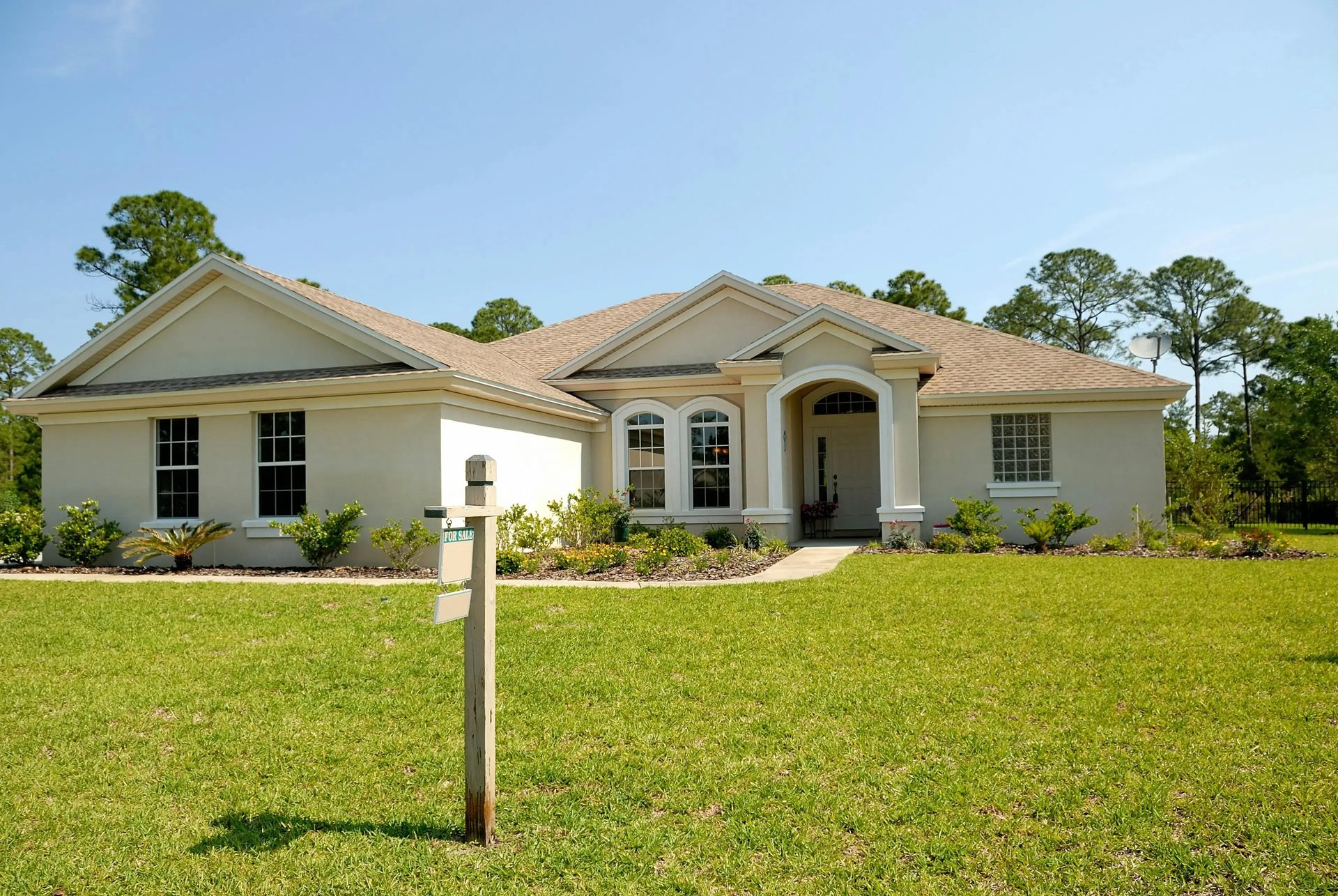 A single-story house with a for-sale sign on the lawn.