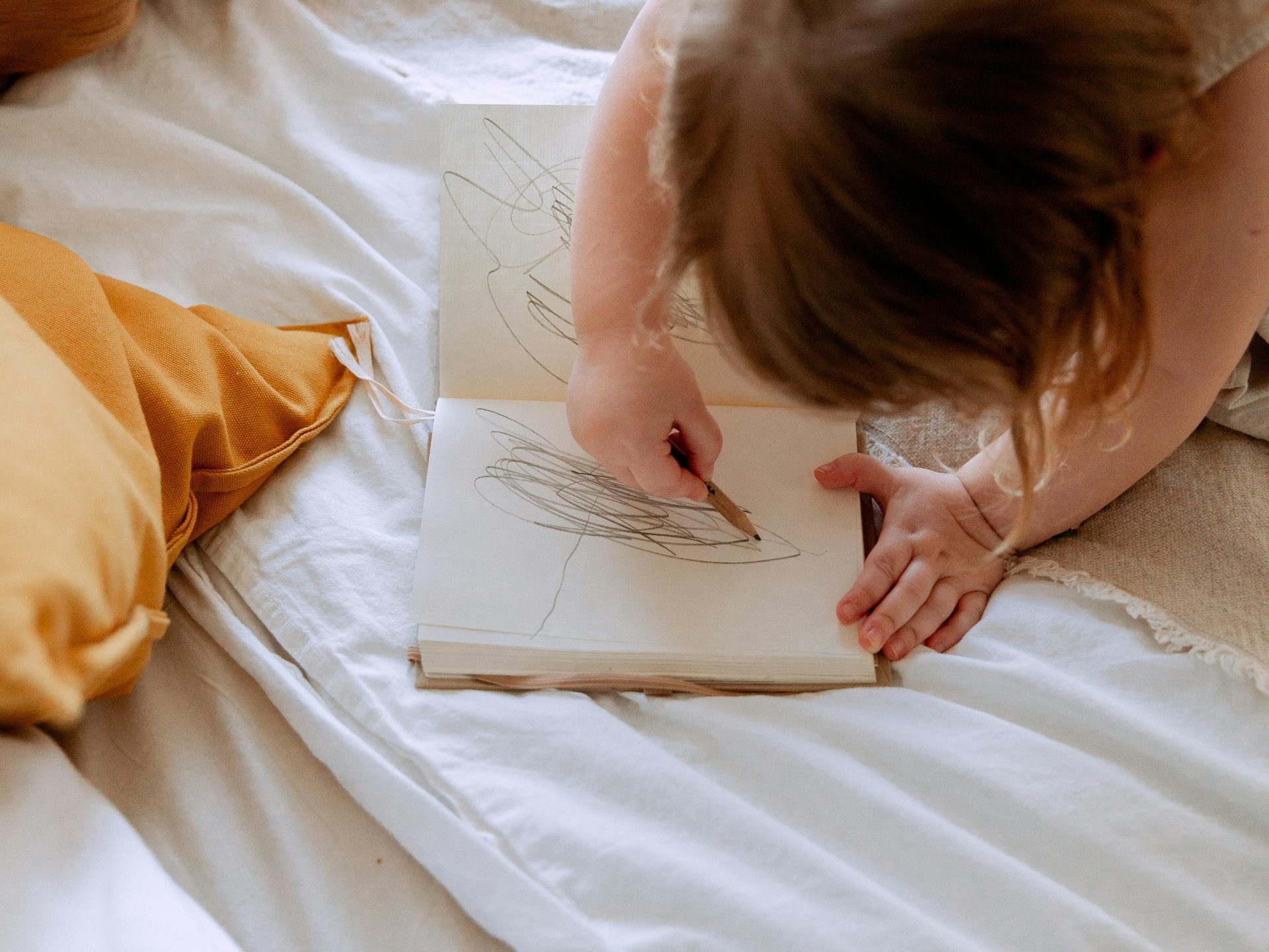 Child drawing in a sketchbook on a bed