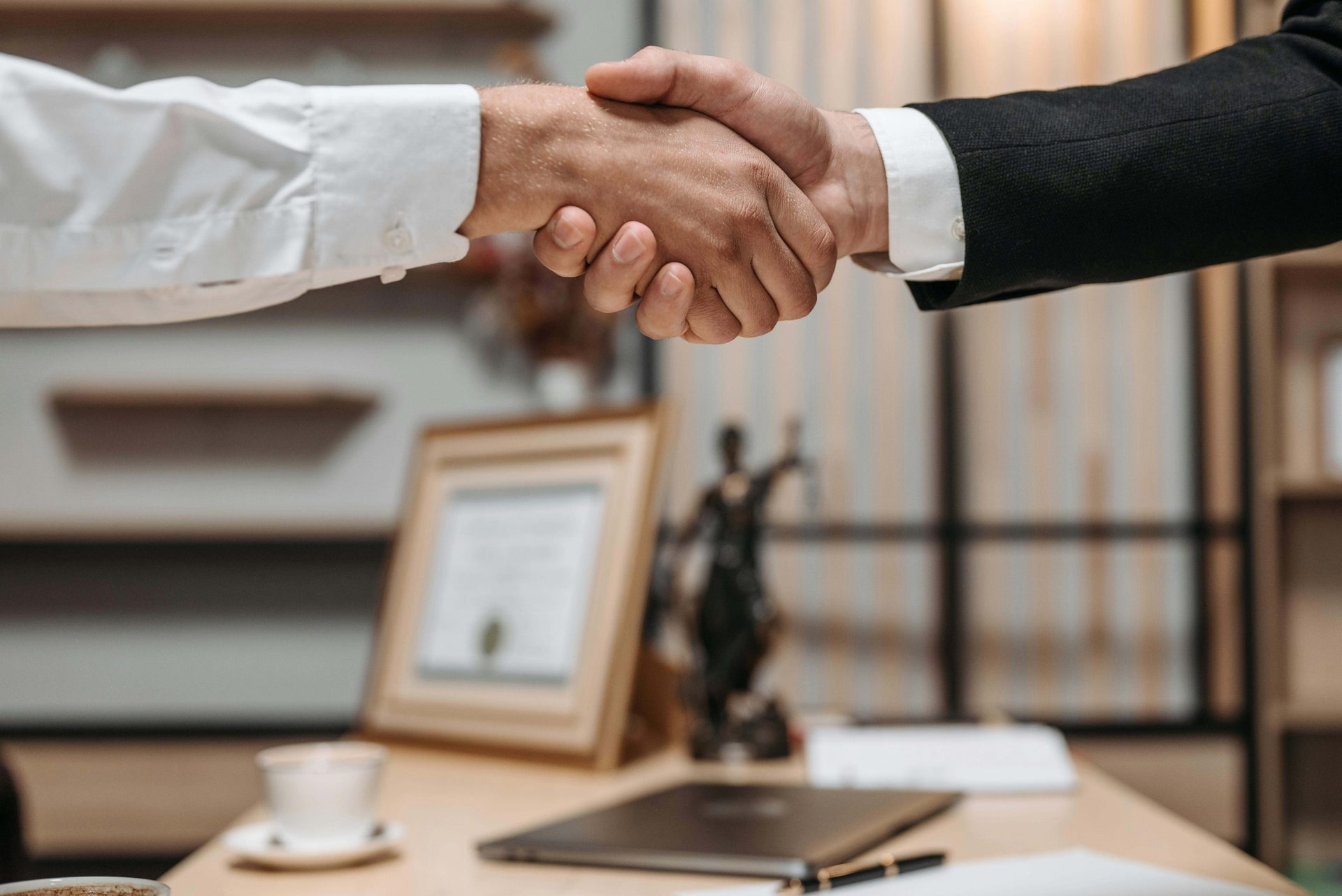 Two people shaking hands above a desk.