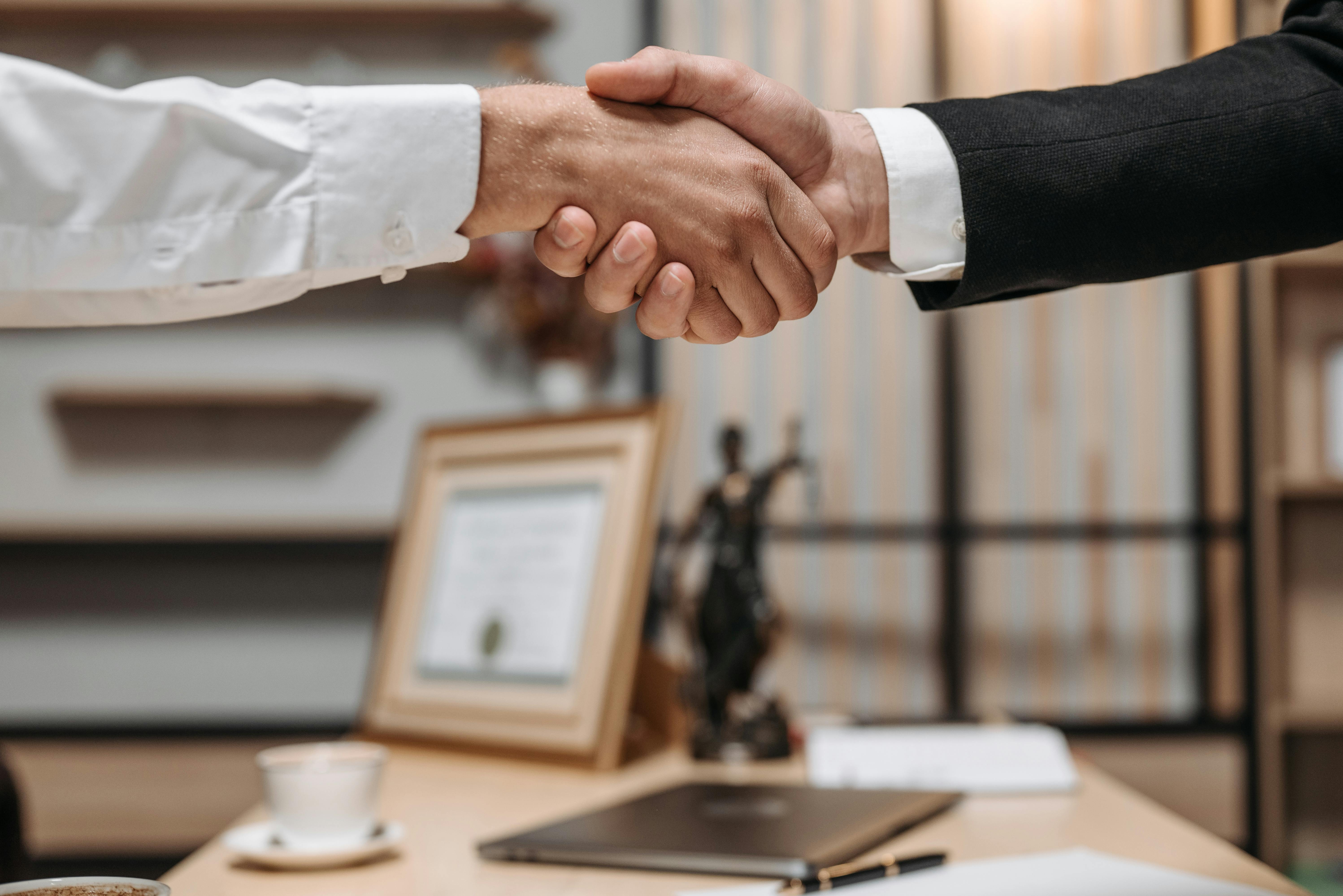 Dos personas estrechándose la mano sobre un escritorio.
