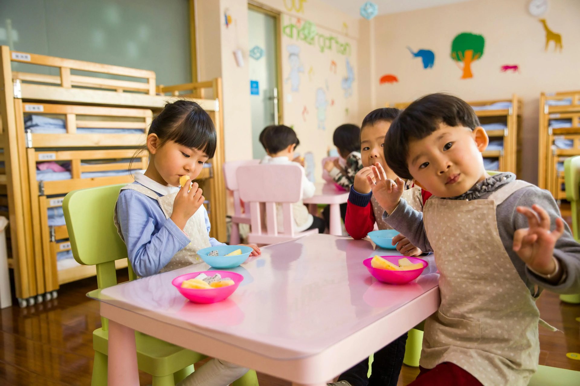 Children eating fruit together at small classroom tables.