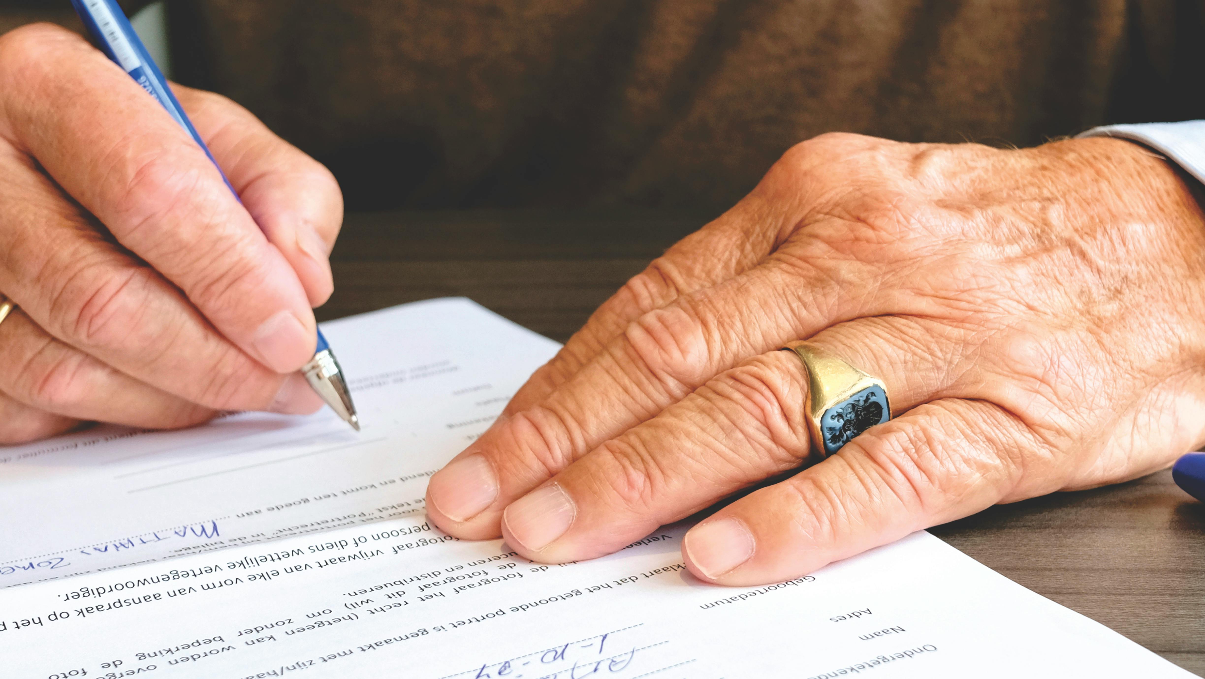 Primer plano de una persona firmando un documento con una pluma azul.