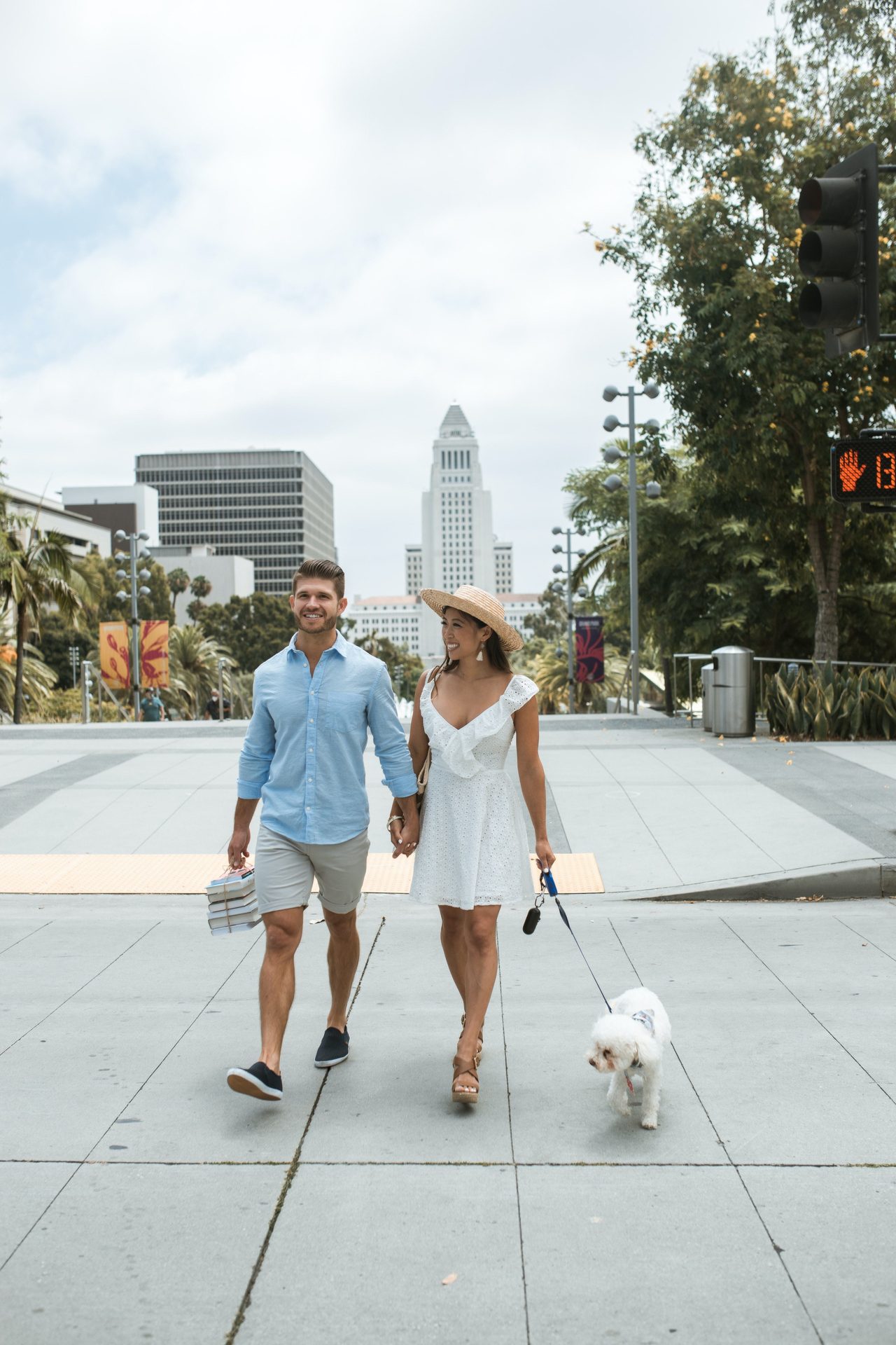 Two adults walking a small white dog on a city sidewalk.