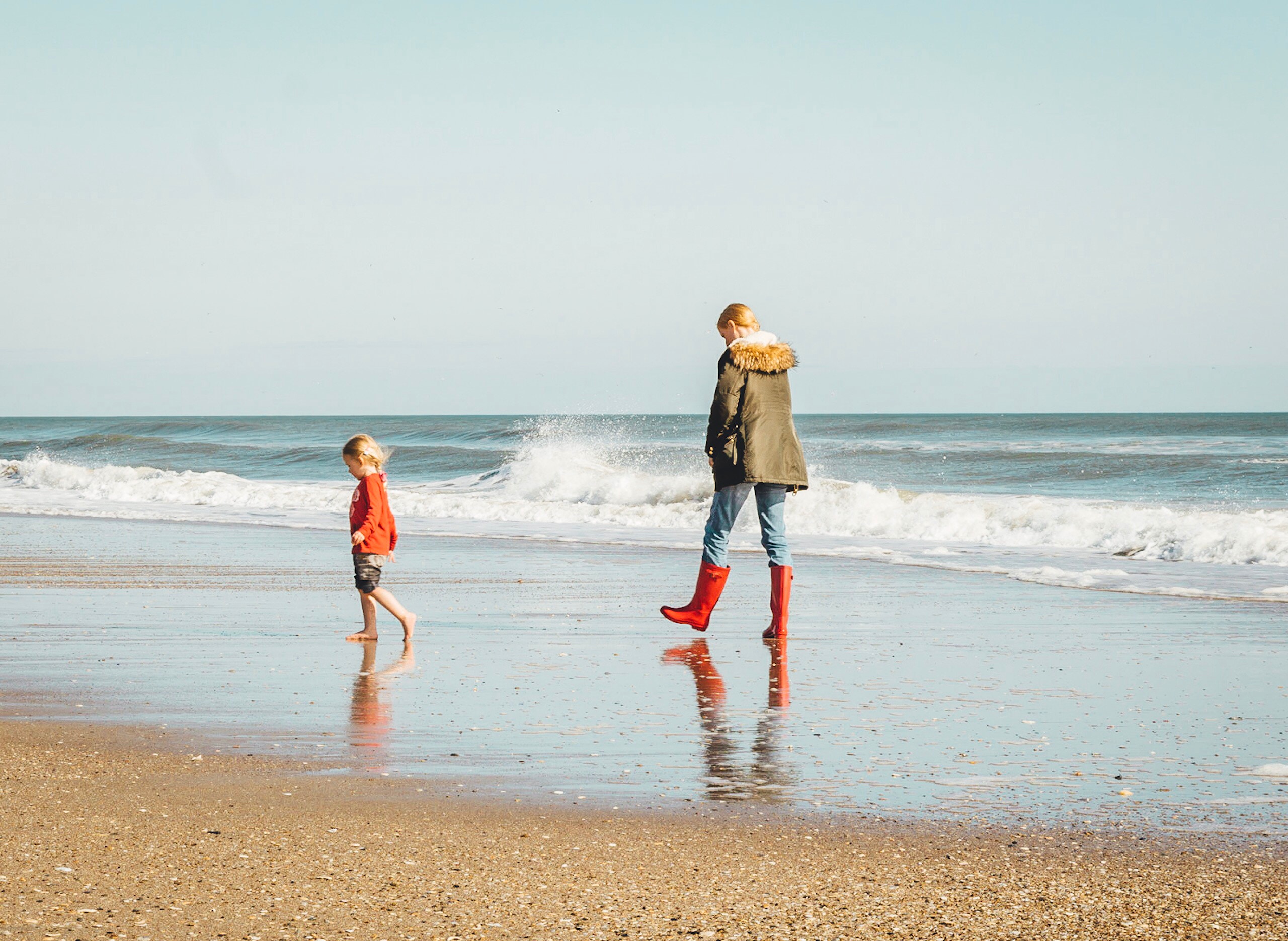 An adult and a child walking along a beach.