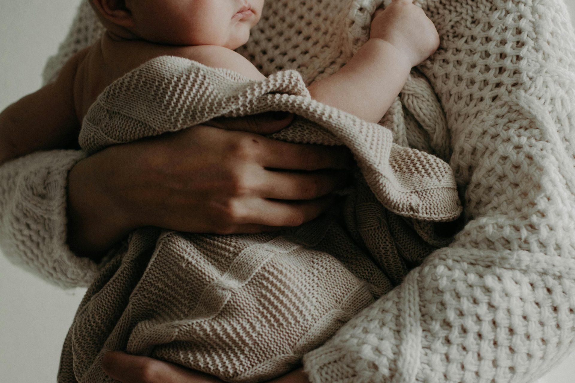 Adult holding a baby wrapped in a knit blanket