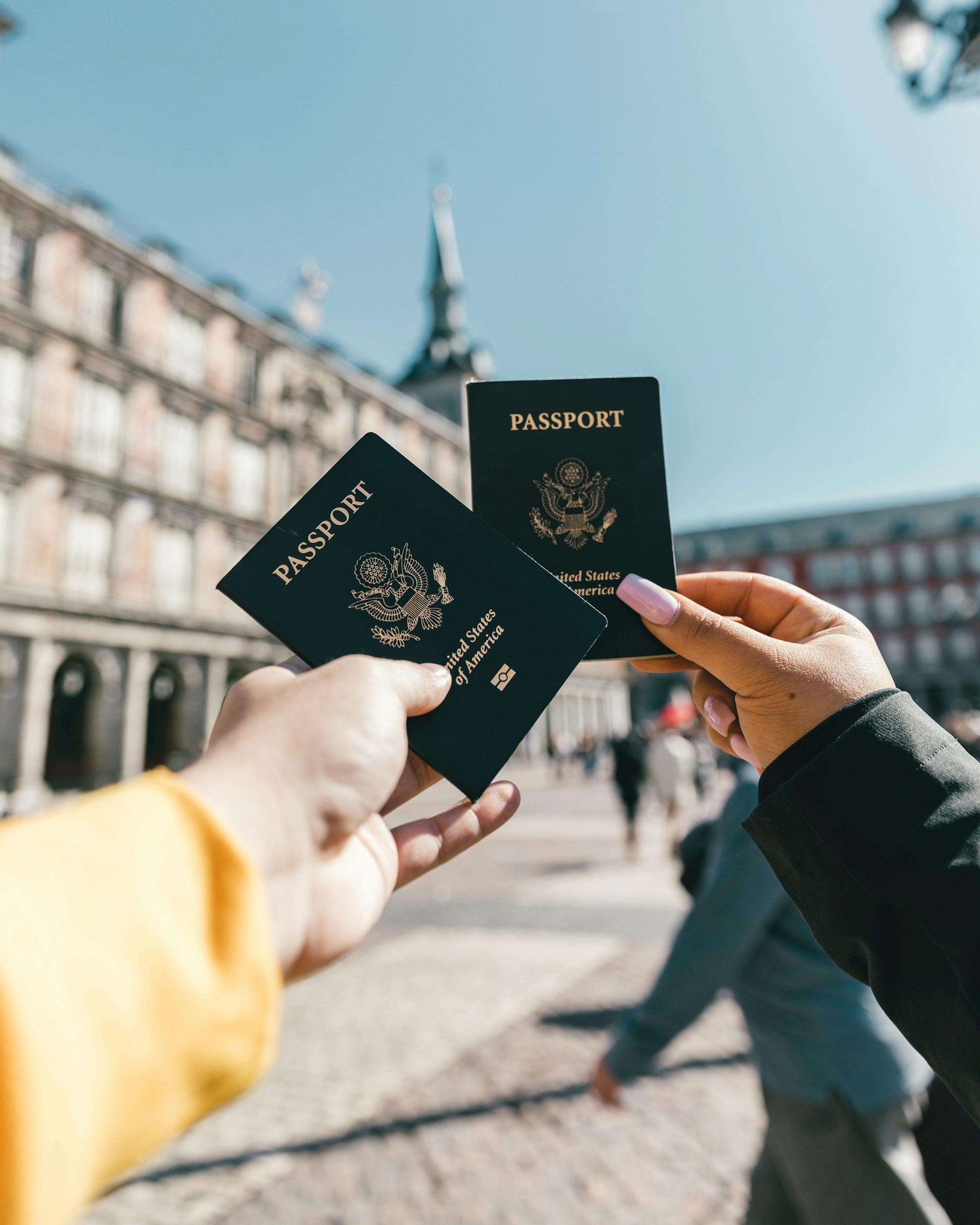 Dos manos sostienen pasaportes de Estados Unidos en una plaza.