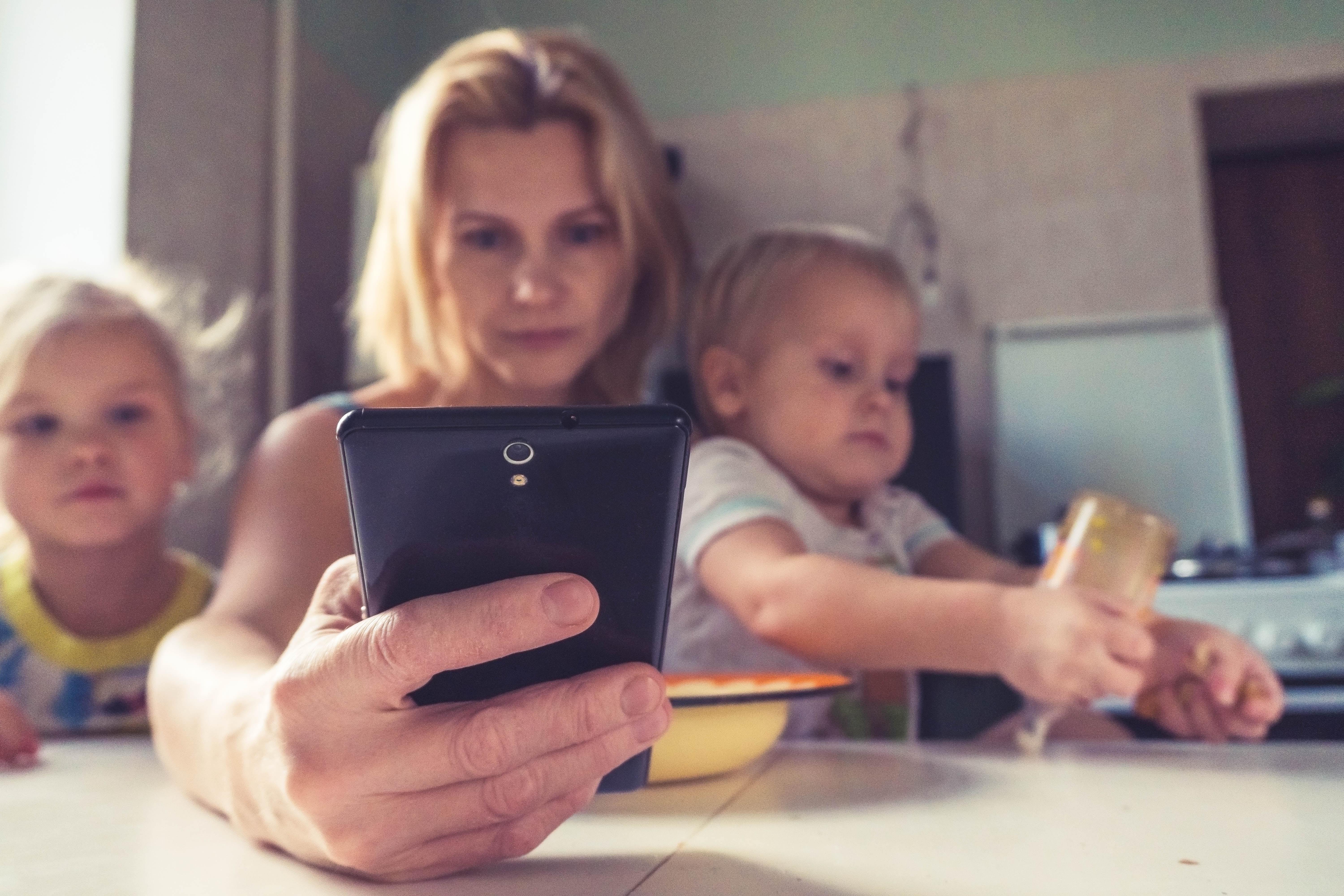 An adult holding a phone with two children nearby.