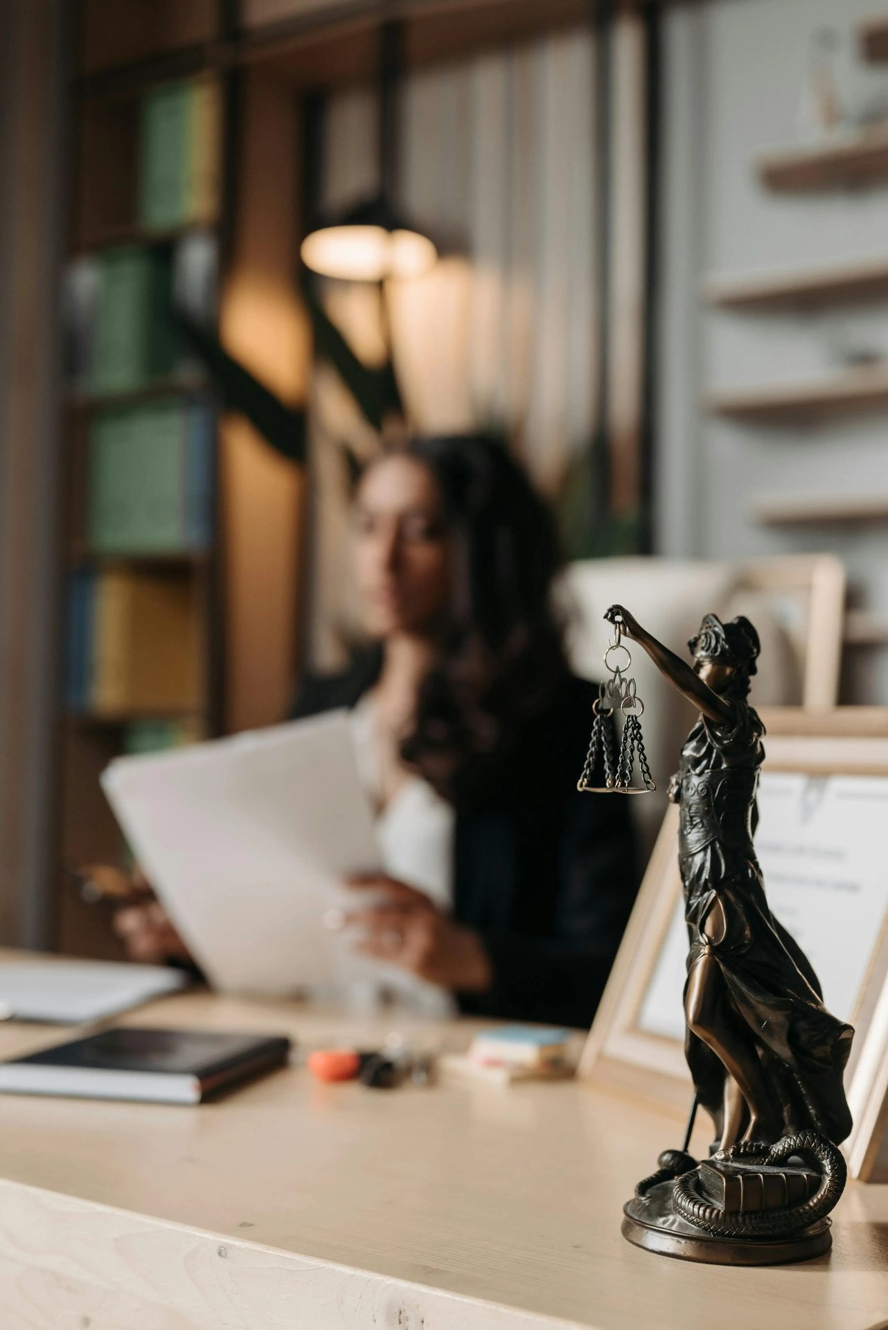 Justice figurine in front of a person reviewing papers at a desk.