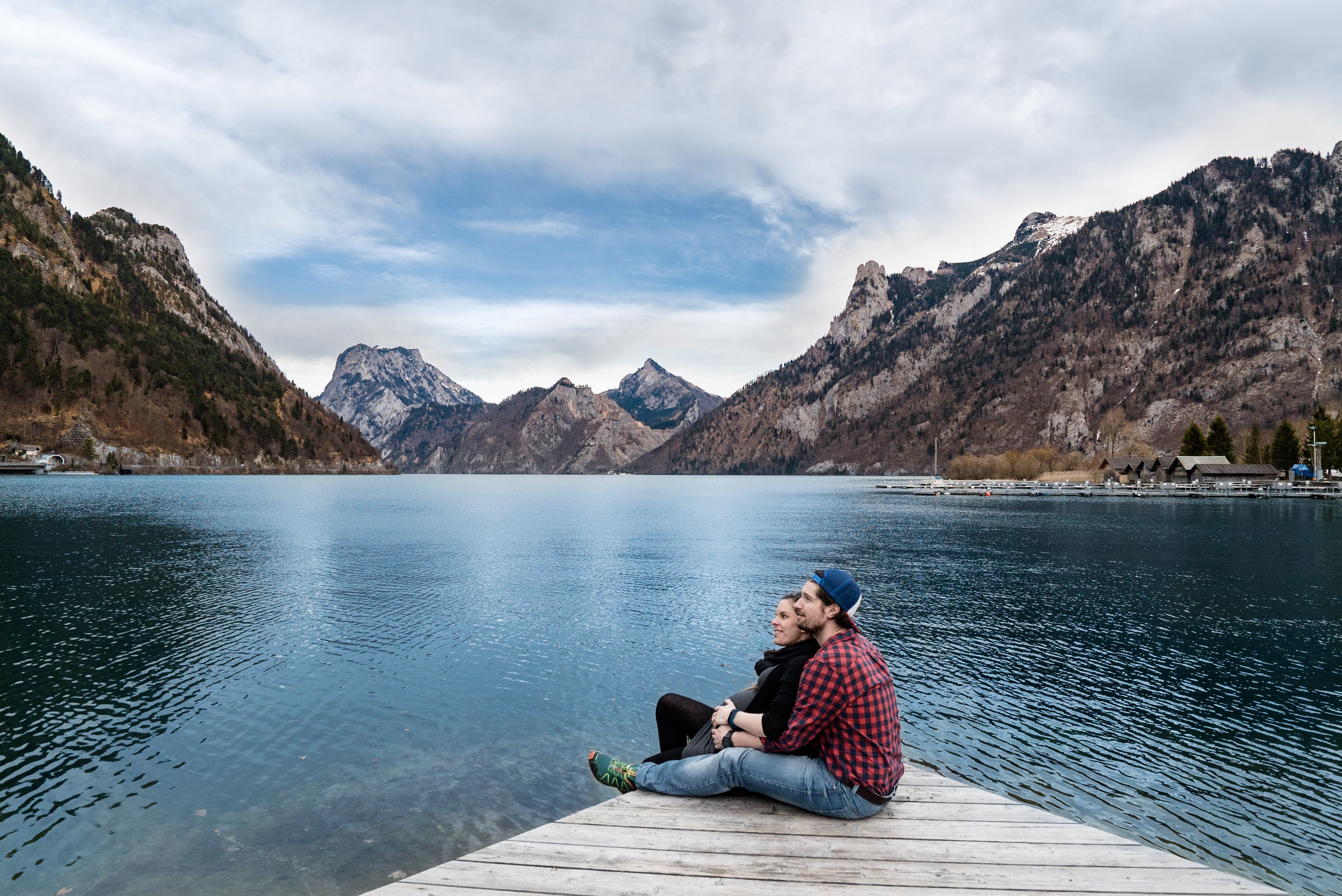 Dos adultos sentados en un muelle junto a un lago de montaña.