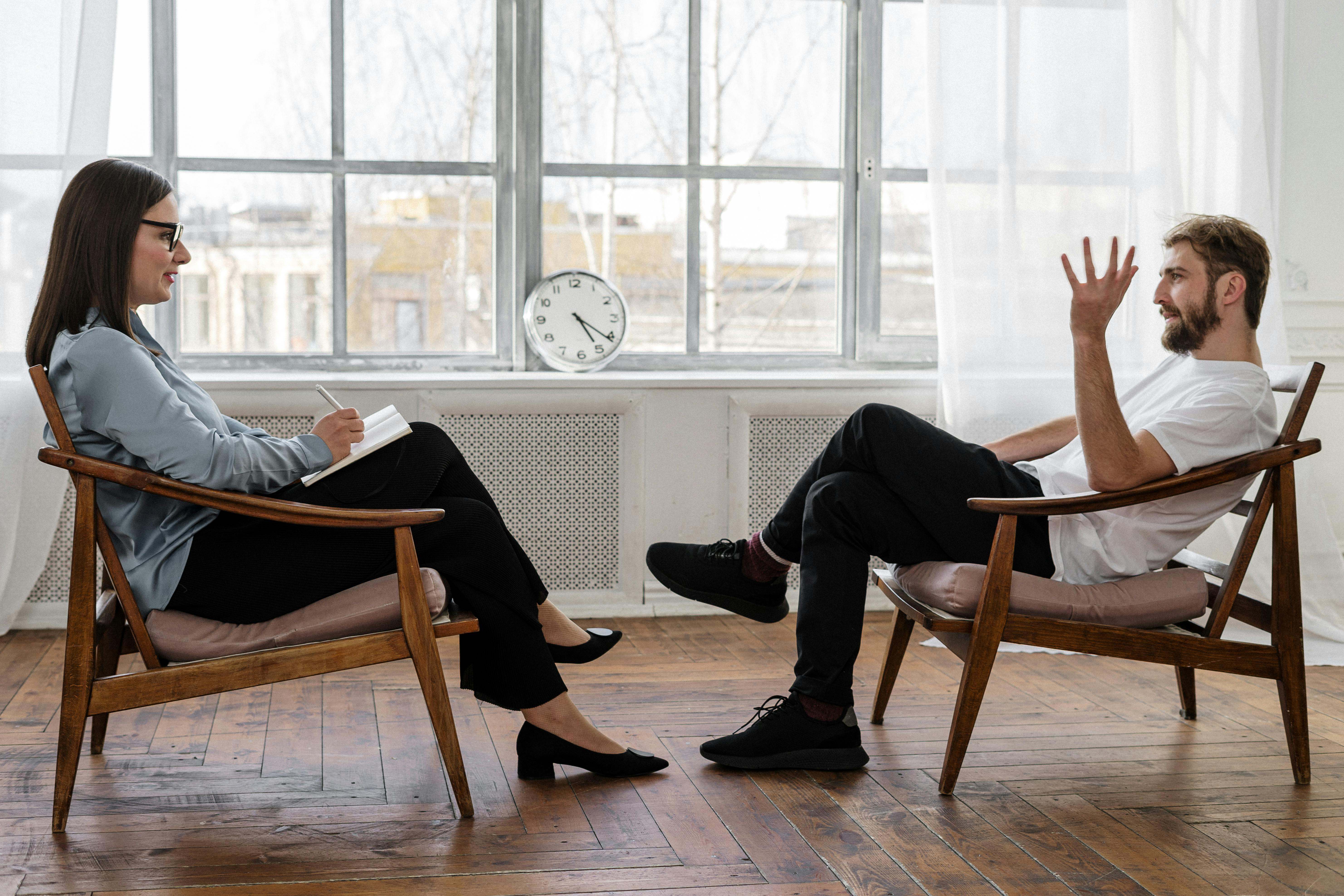 Dos personas hablando en sillones, mientras una toma notas.