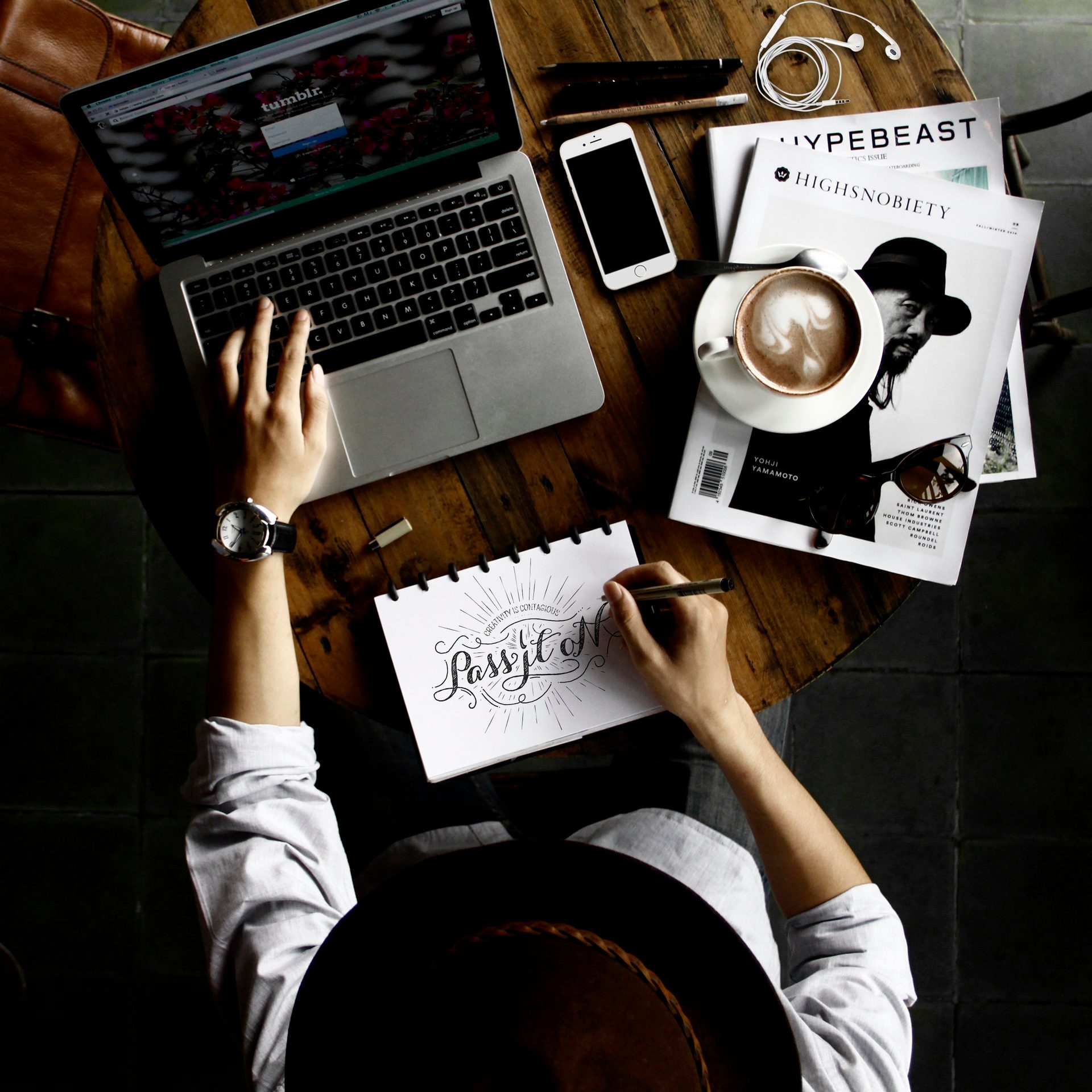 Person writing in a notebook beside a laptop and coffee.